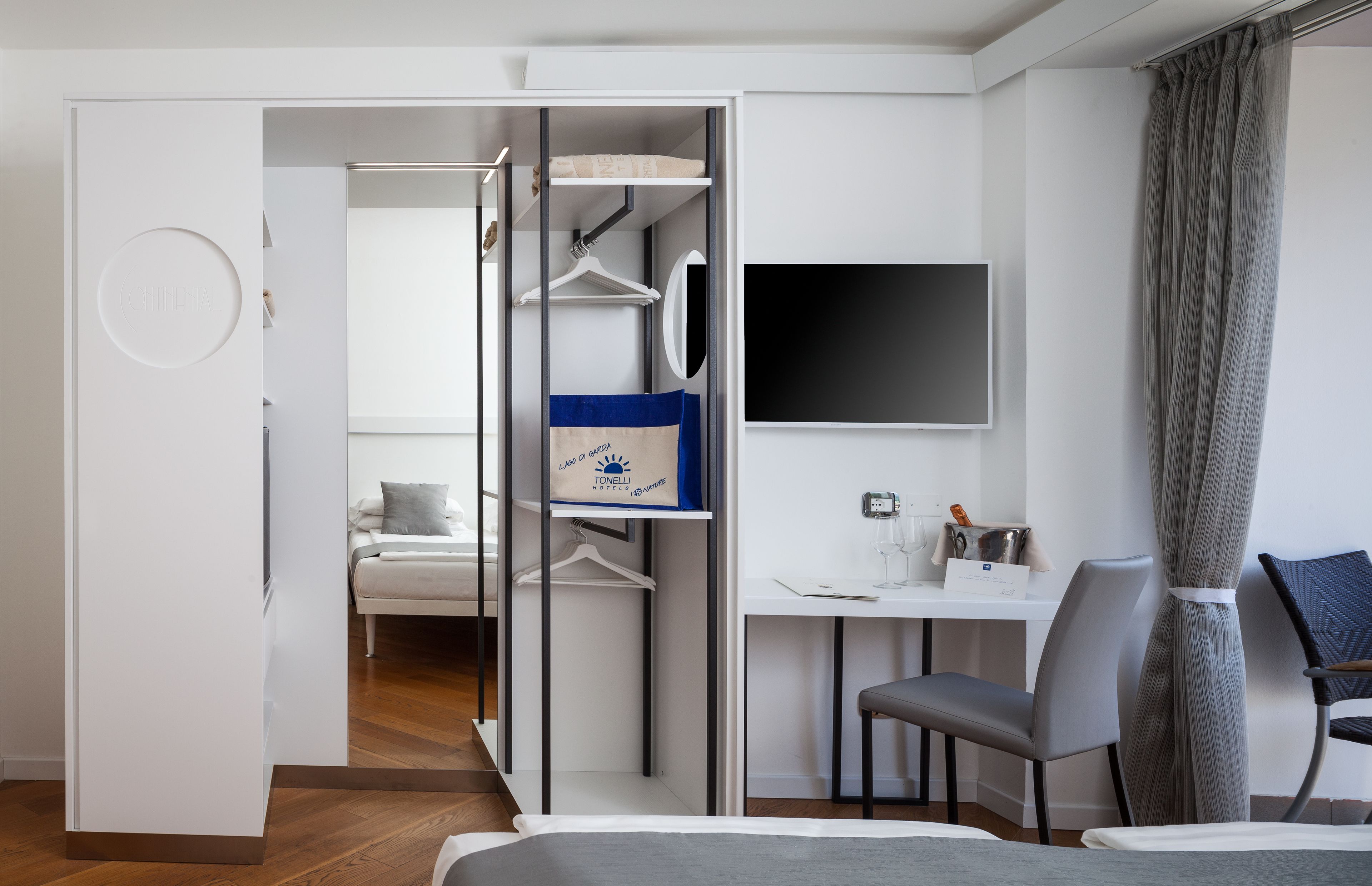 Habitación de hotel moderna con cama, escritorio, silla, televisor y armario con bolso colgando.