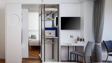 Habitación de hotel moderna con cama, escritorio, silla, televisor y armario con bolso colgando.
