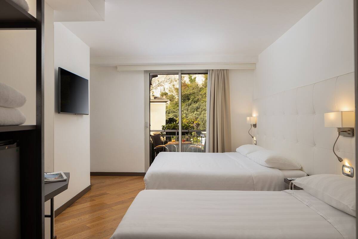 A hotel room with two beds, a TV, and a balcony with outdoor seating.