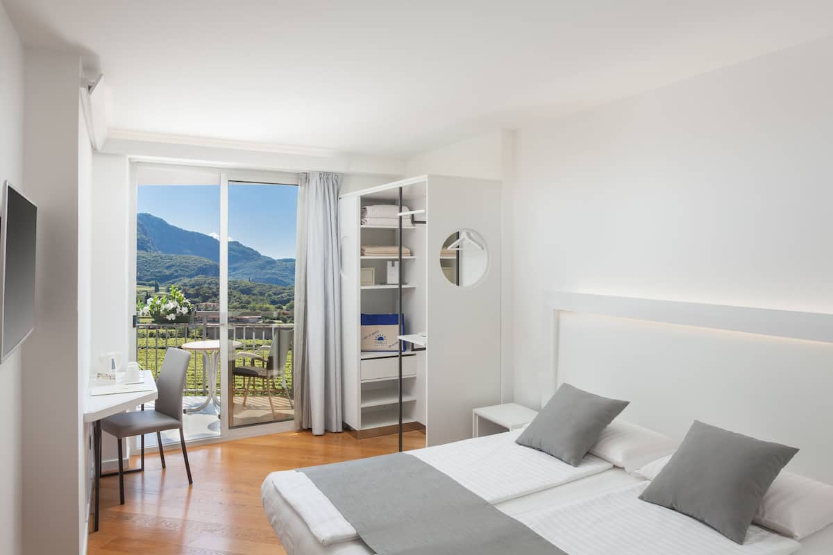 A modern bedroom with a bed, bedside tables, a desk, and a balcony with a mountain view.