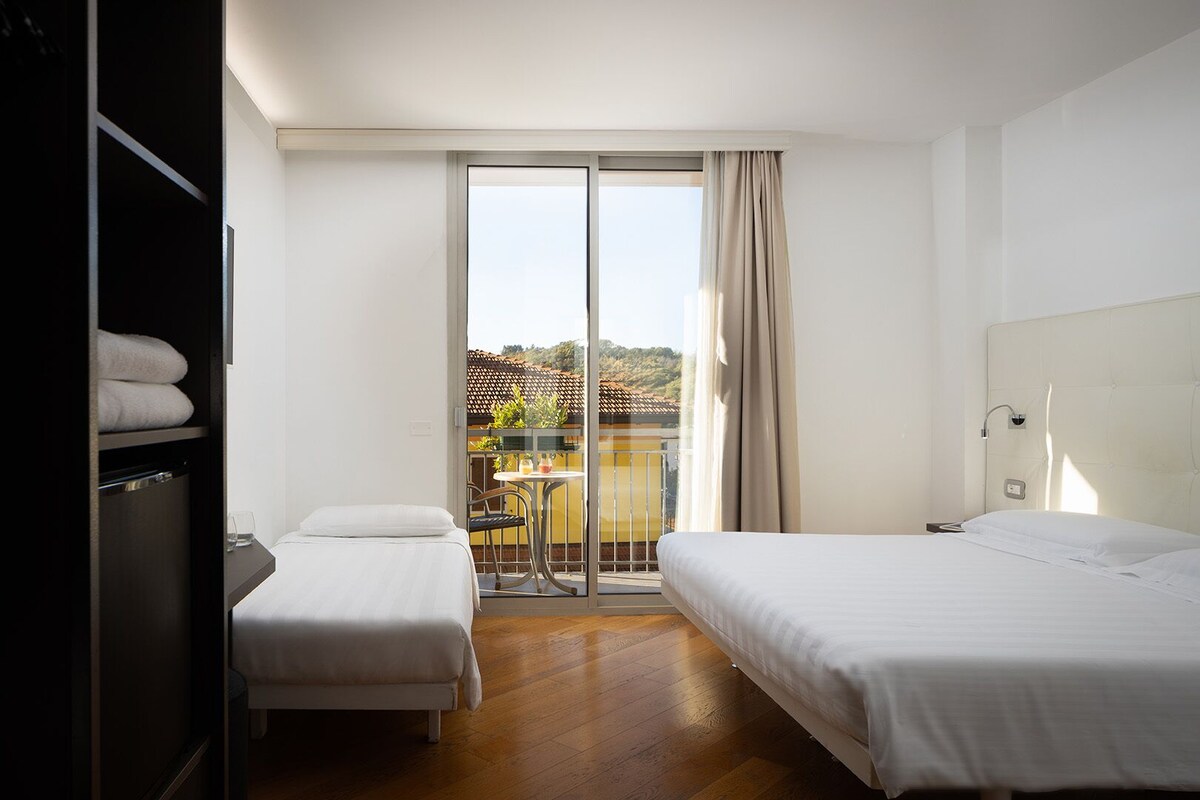 A hotel room with two beds, a balcony with a table and chairs, and a sliding door to the outside.