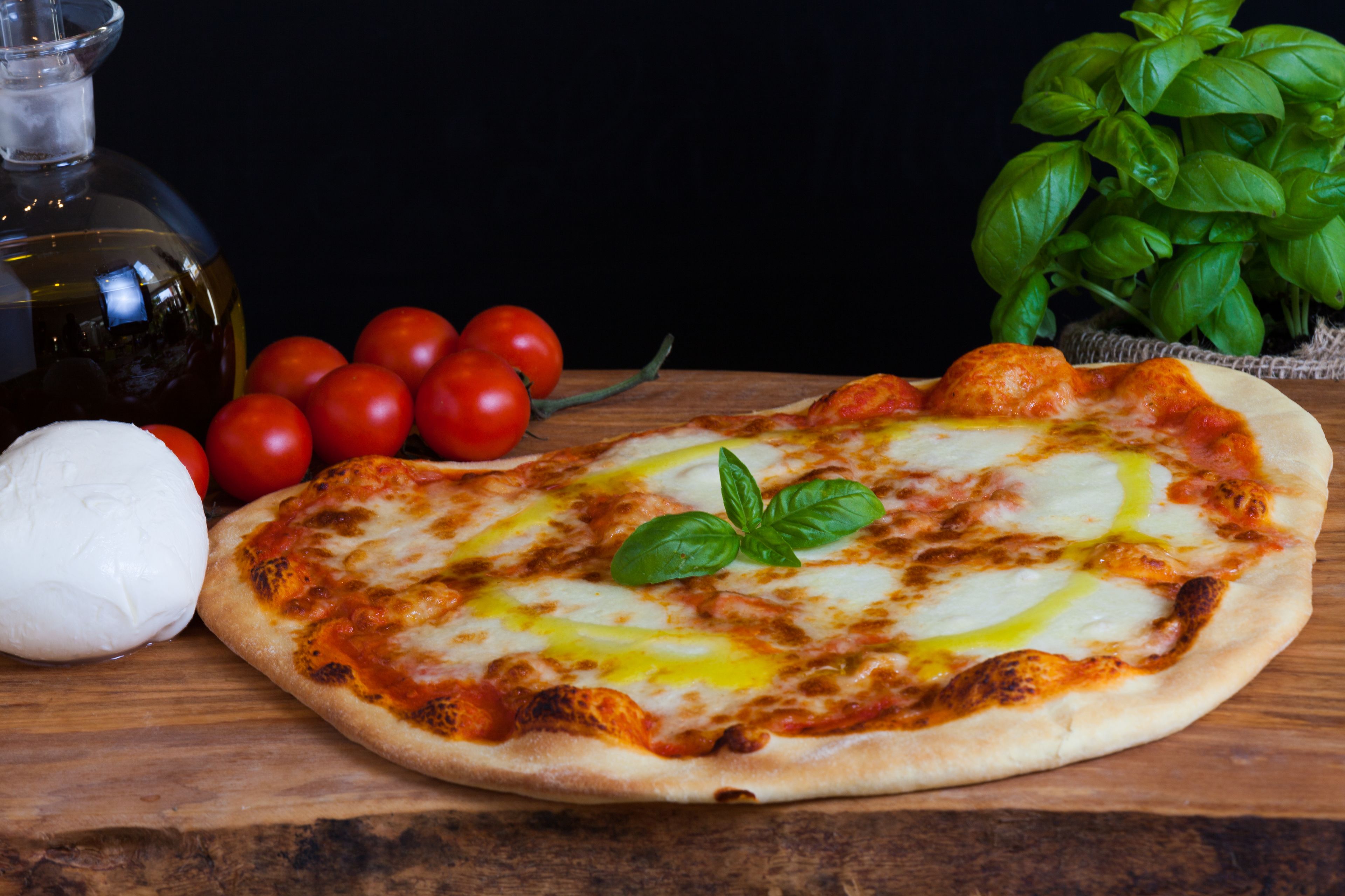 Pizza met kaas en basilicum op een houten ondergrond.