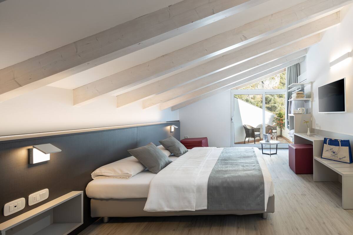 A modern bedroom with a large bed, a TV, and a balcony with a view.