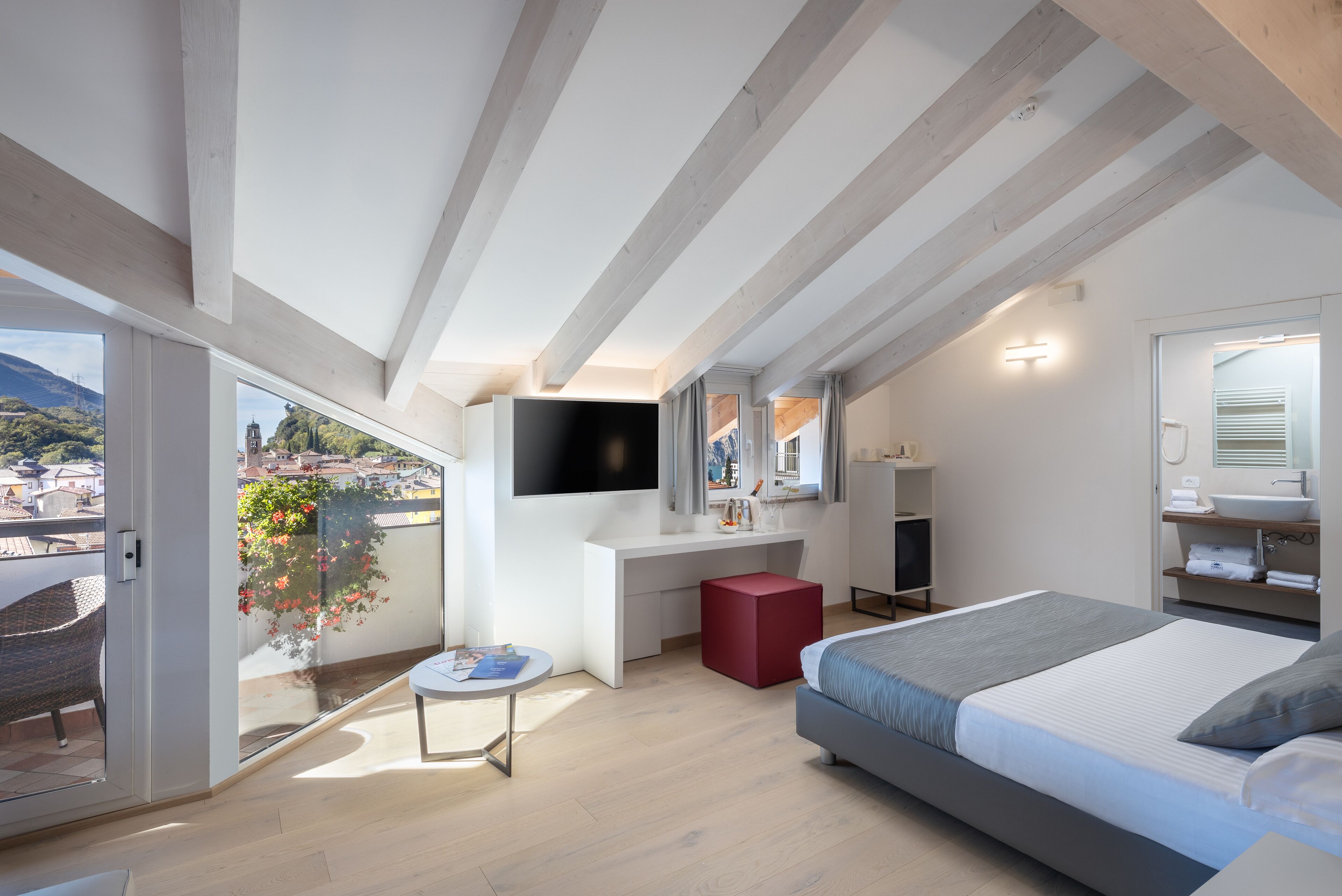 Ein modernes Schlafzimmer mit einem großen Bett, einem Schreibtisch, einem Fernseher und einem Balkon mit Stadtblick.