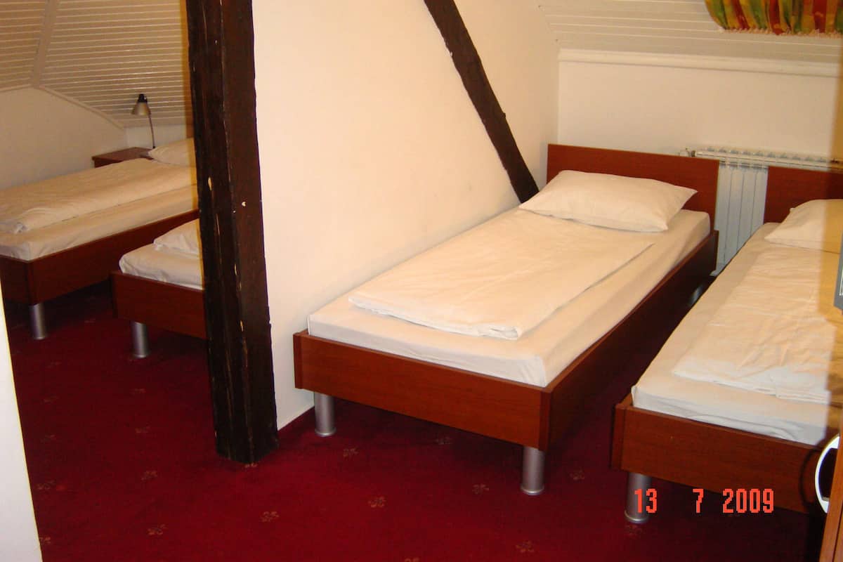 Quarto com três camas de solteiro, cabeceiras de madeira, roupa de cama branca e tapete vermelho.