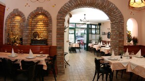 A restaurant with brick arches, tables set with white tablecloths and napkins, and a tiled floor. - Hotel Risnjak (Delnice)