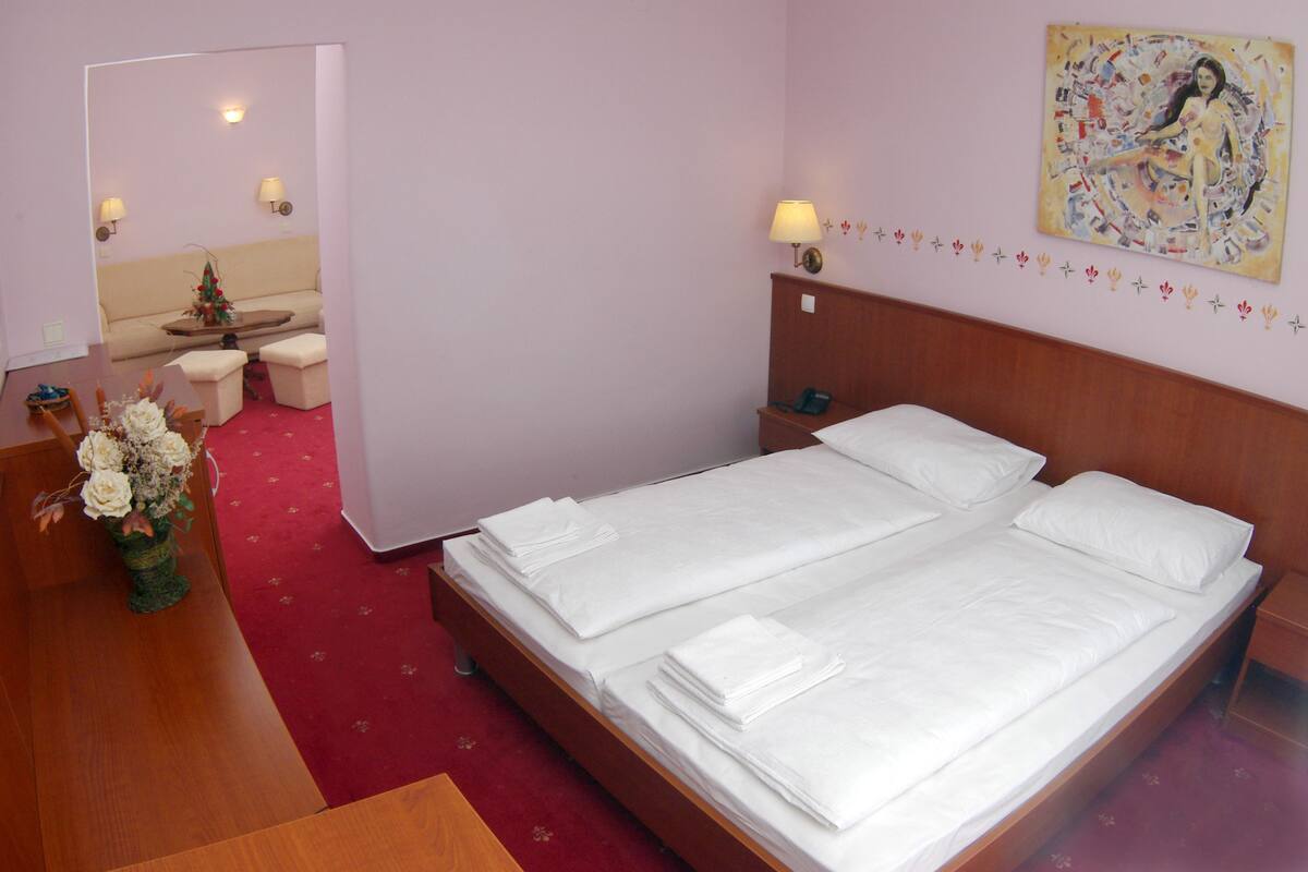 Quarto de hotel com cama de casal, uma mesinha com um vaso de flores, um sofá e duas luminárias na parede.