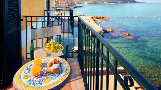A balcony with a table set with food and drinks, overlooking a coastal view with clear water and distant hills. - Villa Sirio (Castellabate)