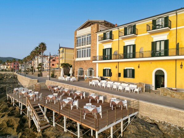 A coastal restaurant with outdoor seating overlooking the beach, featuring a yellow building with balconies and a wooden deck. - Villa Sirio (Castellabate)