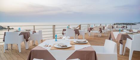A seaside restaurant with tables set for dining, overlooking the ocean.