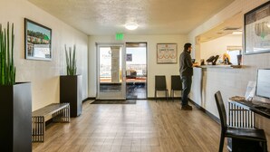 A reception area with a receptionist, a computer, a desk, chairs, a bench, and a door leading outside. - Siegel Select Albuquerque (Albuquerque)