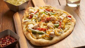 A pizza with various toppings on a wooden board, accompanied by a drink and a salad on a wooden table.