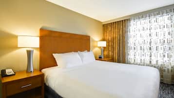 A hotel room with a large bed, two bedside tables with lamps, a wooden headboard, and a patterned curtain.