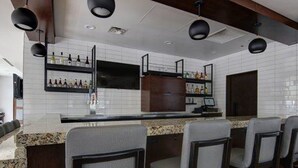 A modern kitchen with a bar area, featuring dark wooden cabinets, white tiled backsplash, and bar stools. - HYATT house Chicago/Naperville/Warrenville (Warrenville)