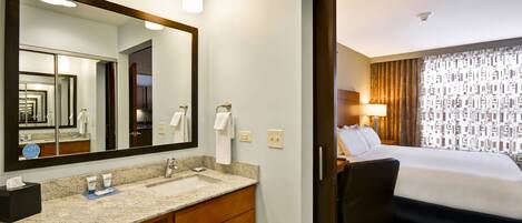 A hotel room with a large mirror, a sink, a chair, and a bed.