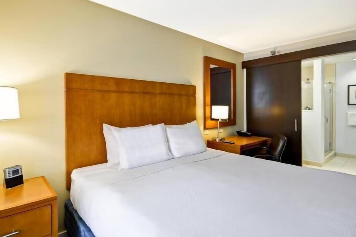 A hotel room with a large bed, bedside tables, a desk, a chair, a lamp, a phone, and a door leading to a bathroom.