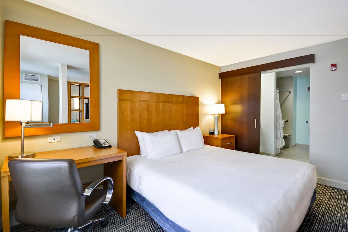 Une chambre d’hôtel avec un grand lit, un bureau avec une chaise, un miroir et une armoire.
