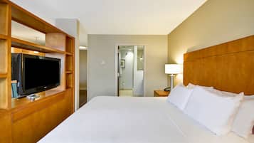 A hotel room with a large bed, a television on a wooden stand, a bedside table with a lamp, and a mirror in the background.