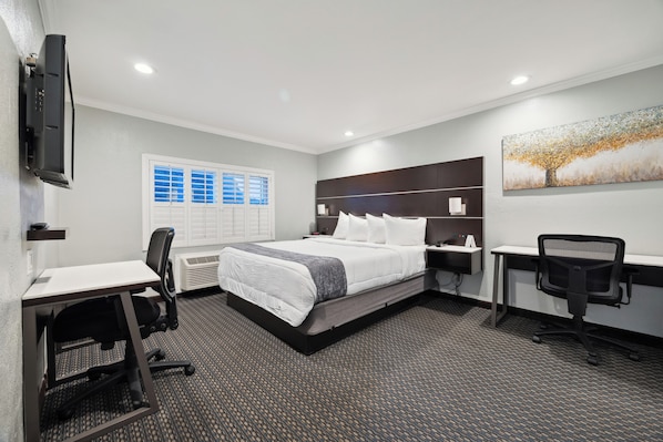 A hotel room with a bed, desk, chair, and a TV mounted on the wall.