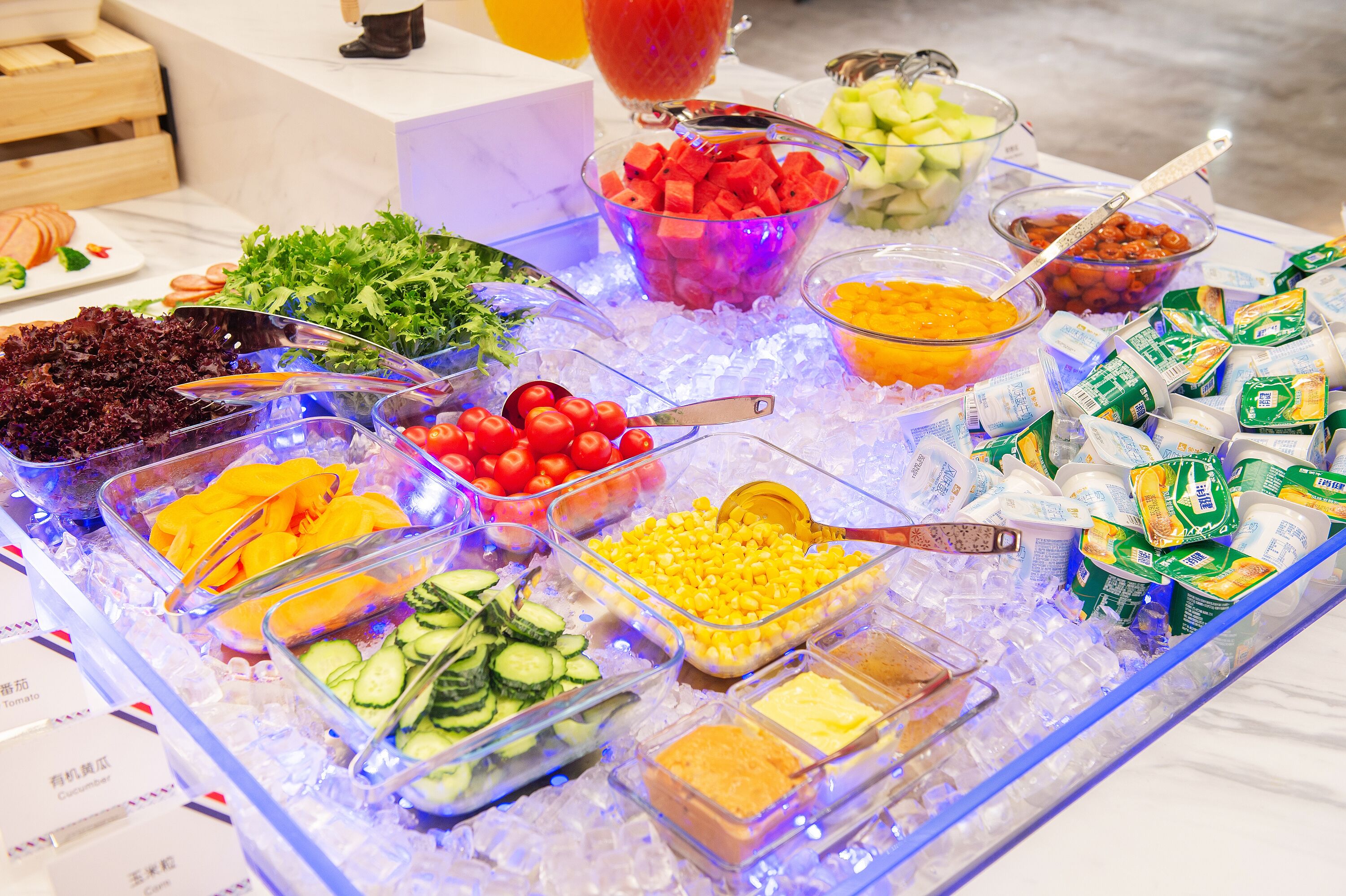 Un bufé con diversos alimentos, como verduras, frutas y productos lácteos, exhibidos sobre hielo.