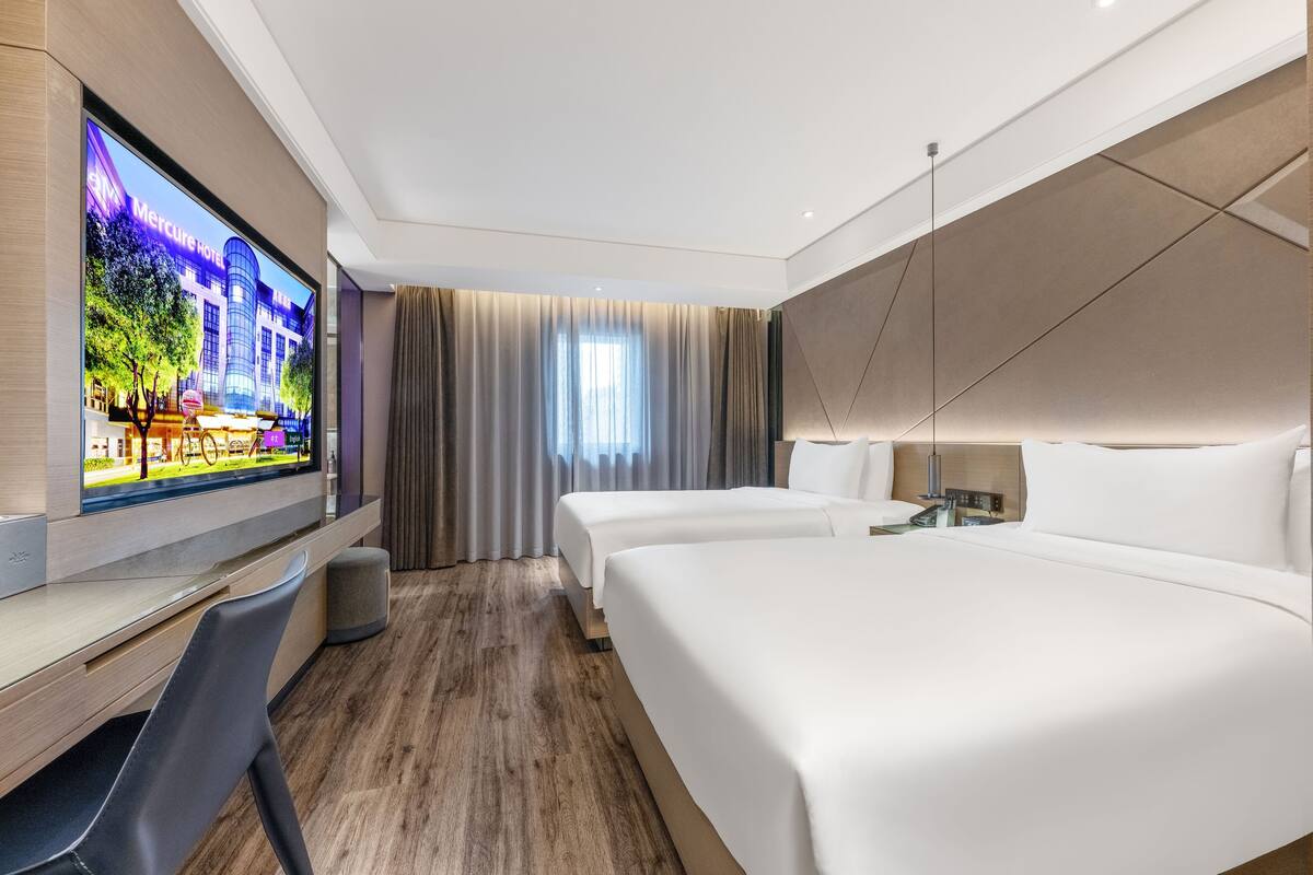 A hotel room with a TV, two beds, a desk, and a chair.