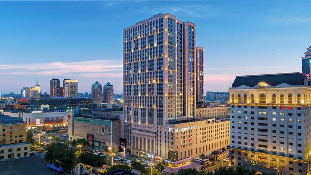 A high-rise building with a grid-like facade, surrounded by other buildings and a busy street. - Mercure Harbin Central Street Sophia Church (Harbin)