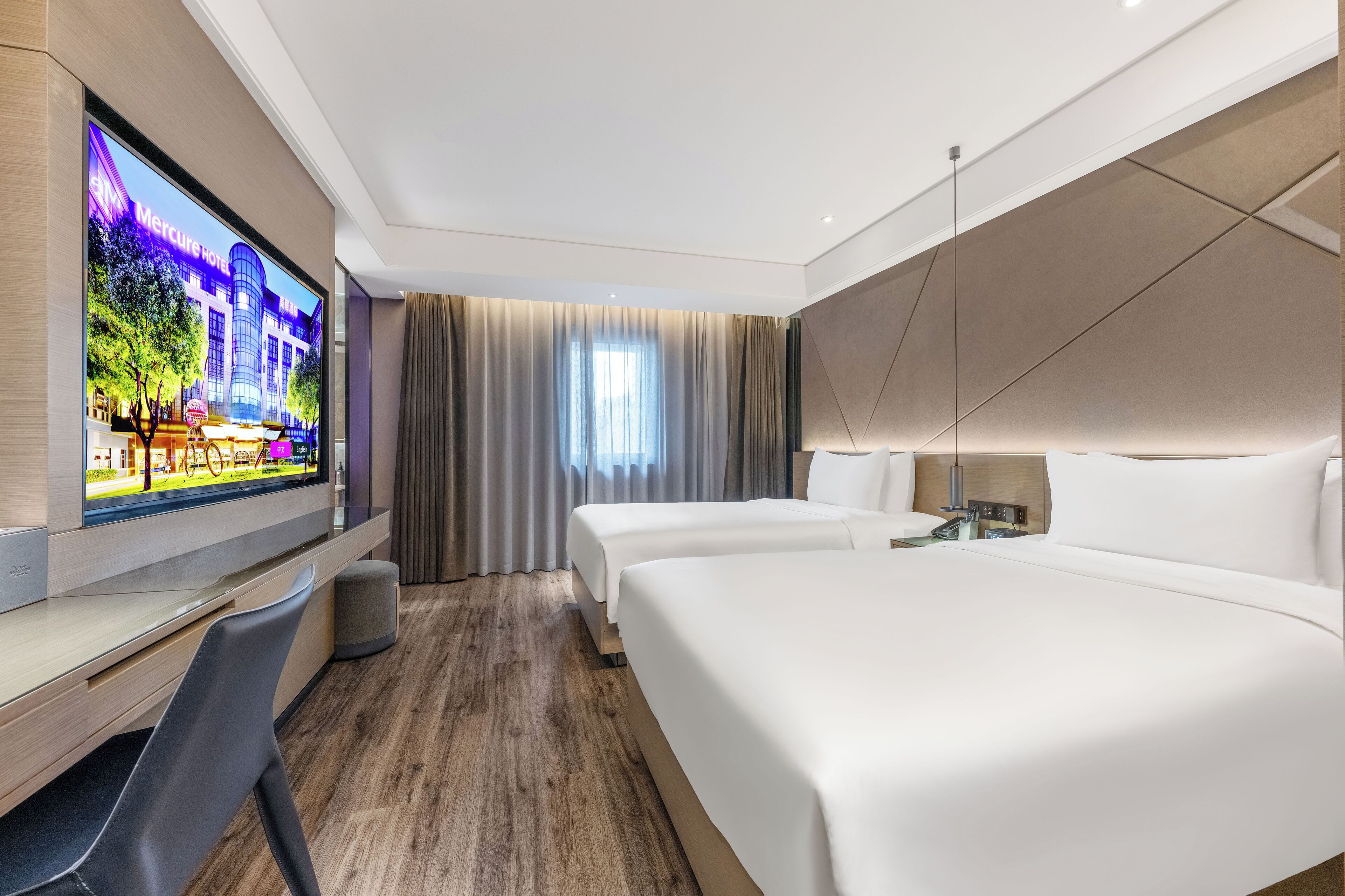 A hotel room with a TV, two beds, a desk, and a chair.