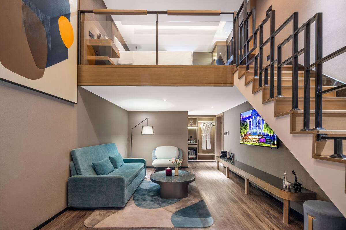 A modern interior with a loft-style staircase, a living area with a sofa and coffee table, and a TV mounted on the wall.