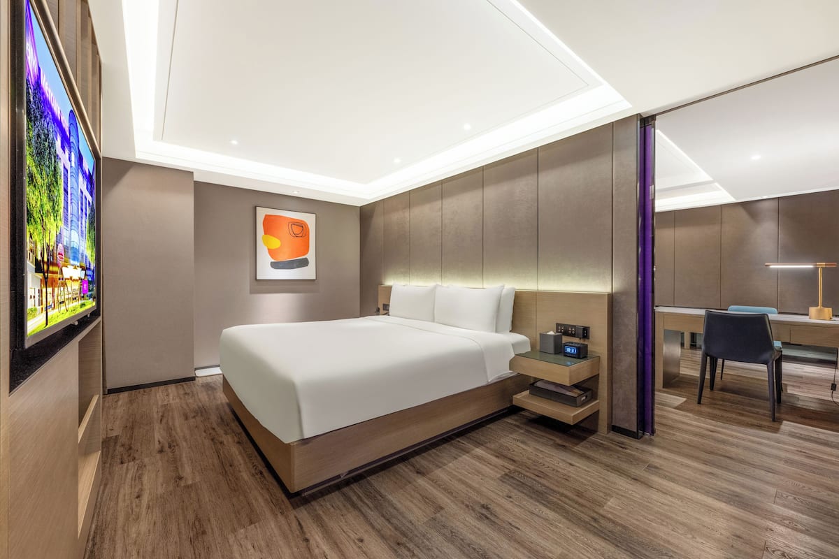 A modern hotel room with a large bed, a desk, and a TV mounted on the wall.