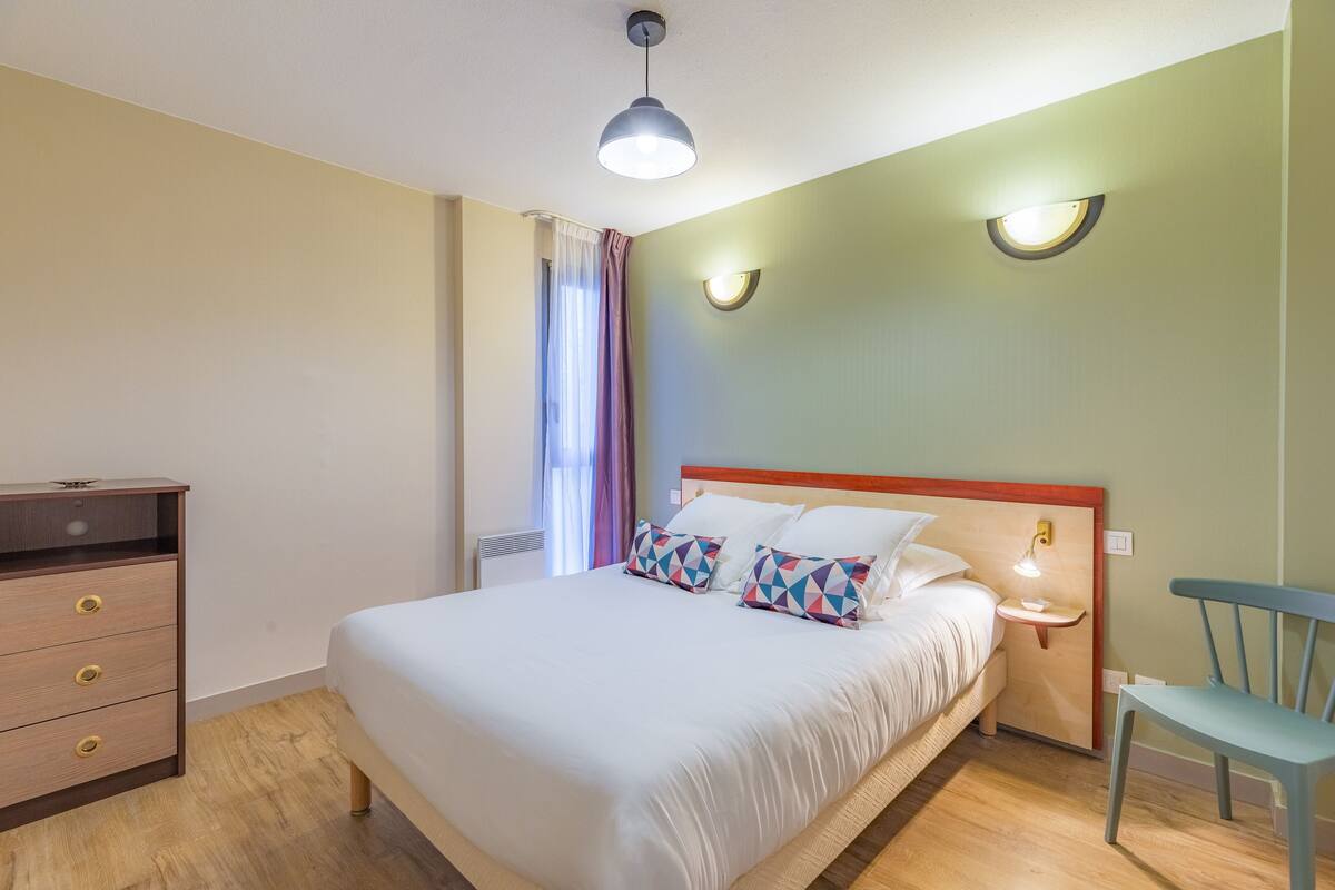 Un dormitorio ordenado con cama, mesita de noche, silla y cómoda.