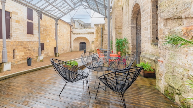 An indoor courtyard with stone walls, a glass roof, and a wooden floor. There are metal chairs and tables arranged for seating. - Appart'City Classic  Angoulême Centre (Angouleme)