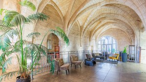 A spacious lobby with high arched ceilings, a large potted plant, seating area, and a view through a large window. - Appart'City Classic  Angoulême Centre (Angouleme)