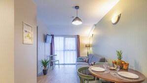 A dining area with a round table set for two, a sofa, and a TV mounted on the wall. - Appart'City Classic  Angoulême Centre (Angouleme)