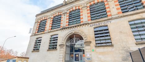 A historic building with a prominent entrance, large windows, and a sign reading "APPARTCITY".
