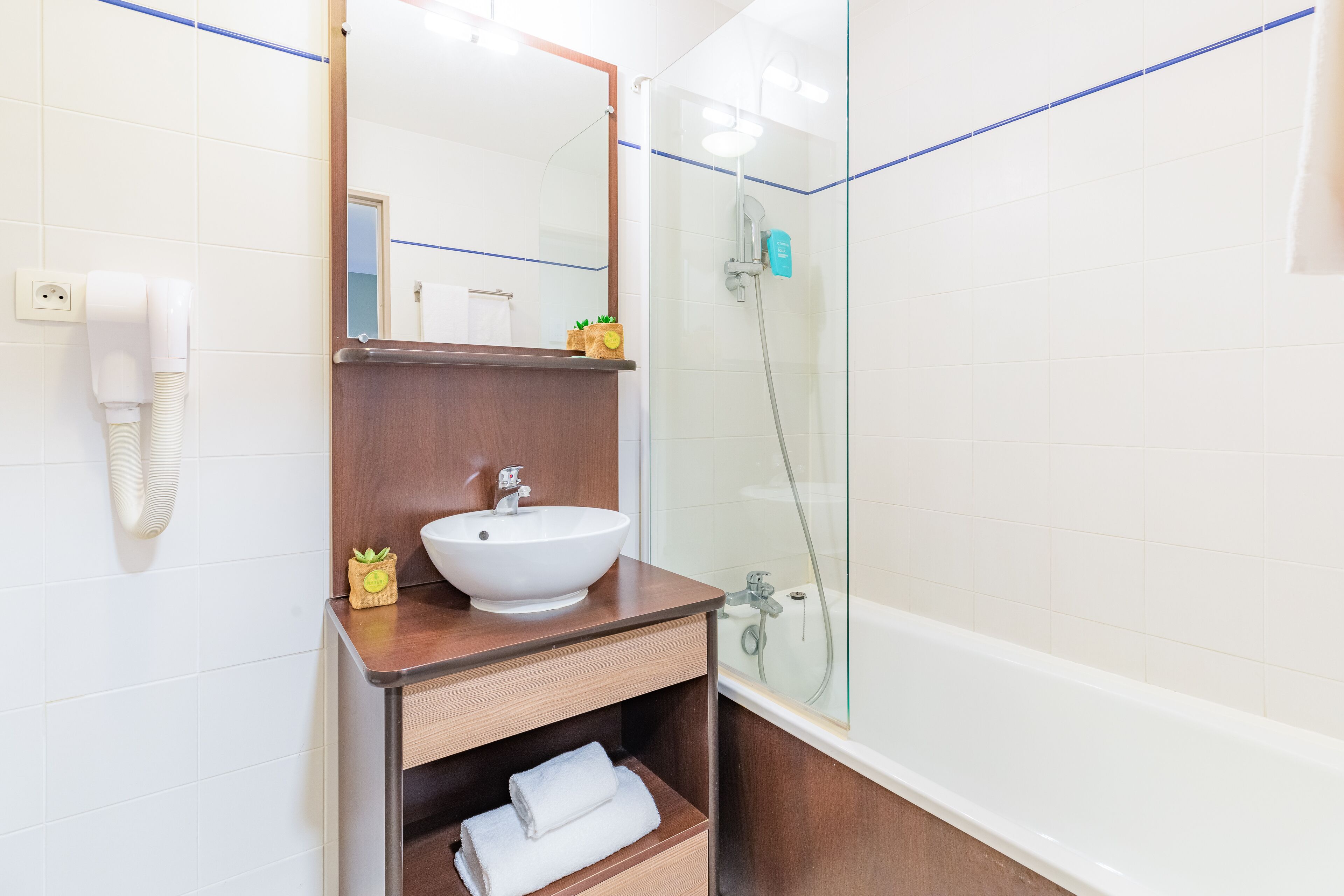 A modern bathroom with a wooden vanity, a white sink, a mirror, and a glass-enclosed shower area.