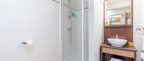 Un baño moderno con ducha envuelta en vidrio, un lavamanos blanco y un mueble de tocador de madera.