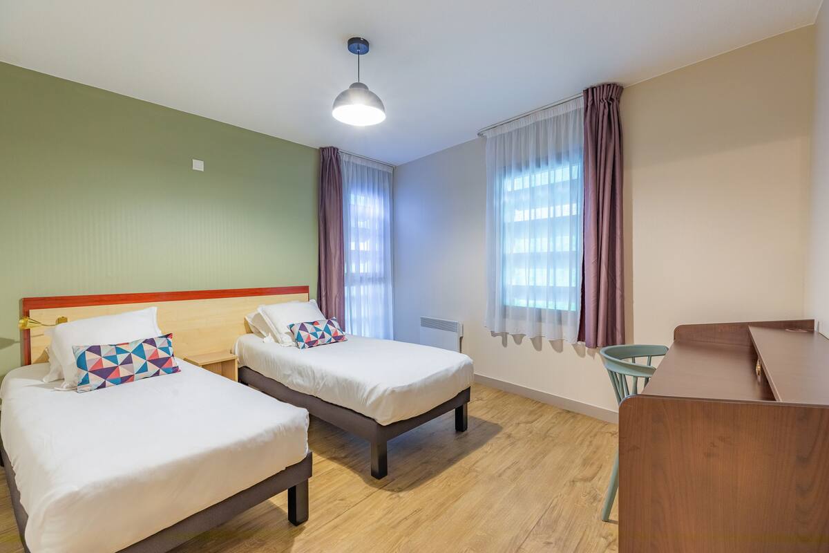 Una habitación de hotel con dos camas, suelo de madera, un escritorio y una silla.