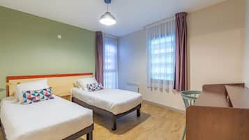 A hotel room with two beds, a wooden floor, a desk, and a chair.