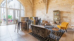 A spacious interior with a high arched ceiling, rustic stone walls, and a large glass door leading outside. Furnishings include a round table, bar stools, and a yellow armchair. - Appart'City Classic  Angoulême Centre (Angouleme)