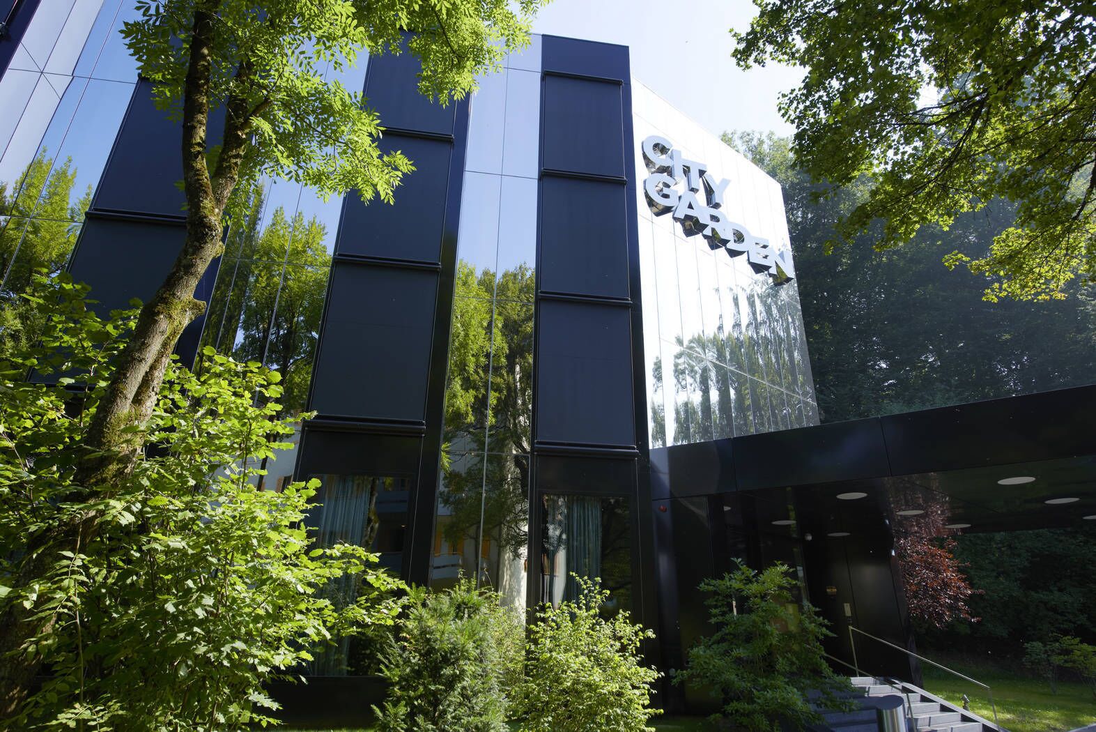 A modern building with a reflective glass facade and a sign that reads "City Garden."