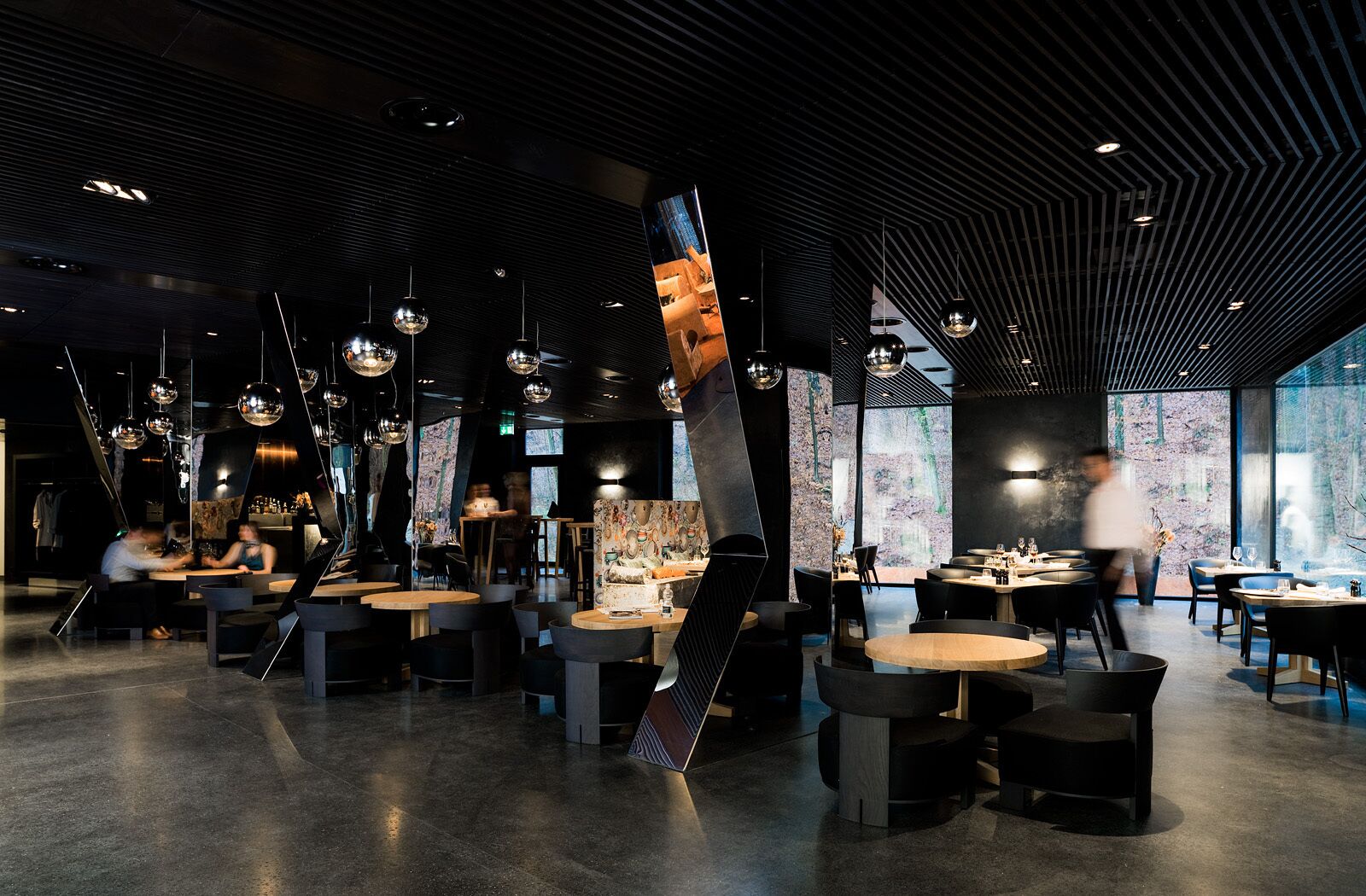 Un restaurante moderno con techos altos, esferas colgantes como luces y una combinación de mesas redondas y rectangulares.