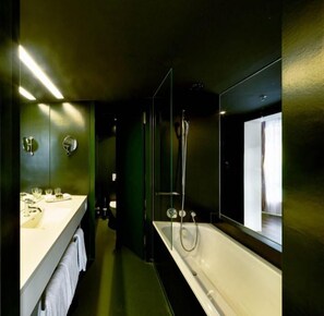 A modern bathroom with a large bathtub, a vanity with a mirror, and a shower area. - City Garden Hotel (Zug)