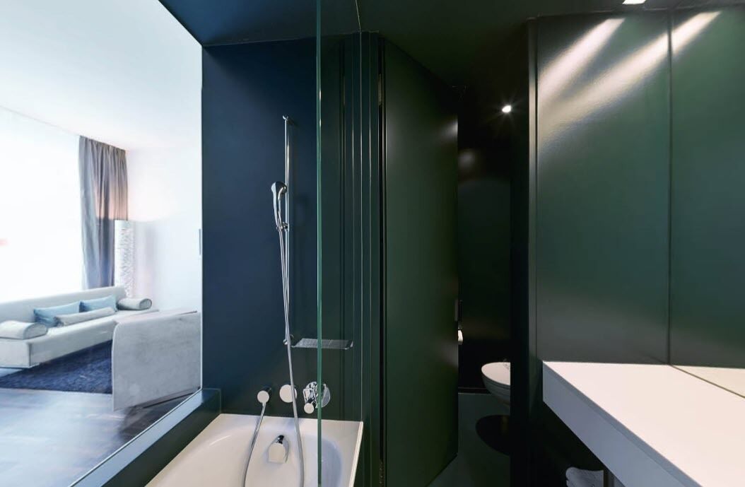Un baño moderno con ducha de vidrio, lavamanos blanco y pared oscura.