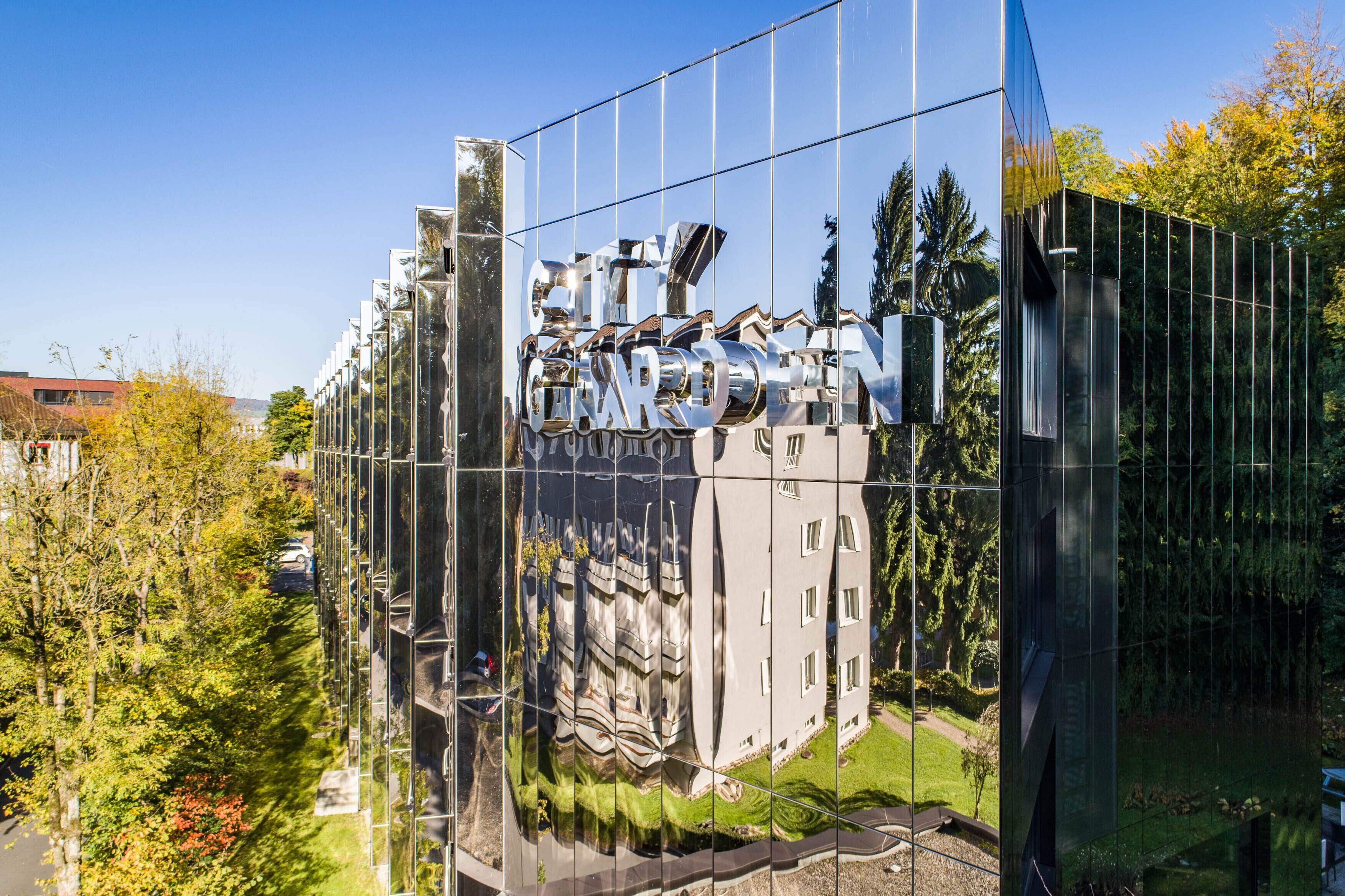 A modern building with a reflective glass facade and a sign that reads "CITY GARDEN".
