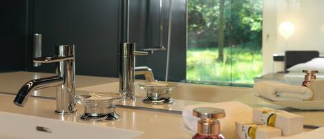 A modern bathroom with a large mirror, two sinks, and a view of greenery outside.