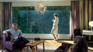 A modern living room with a large window, a sofa, a coffee table, and a chair. - City Garden Hotel (Zug)