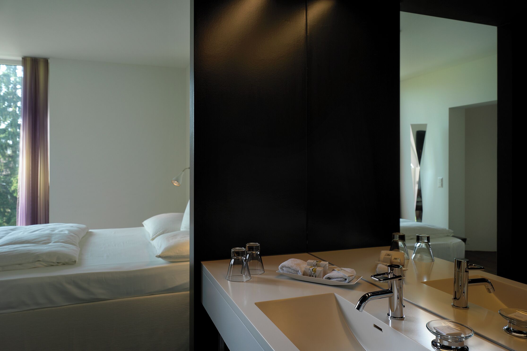 A hotel room with a bed, a bathroom with a sink, and a mirror.