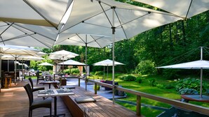 An outdoor dining area with multiple tables and chairs, surrounded by umbrellas and greenery. - City Garden Hotel (Zug)