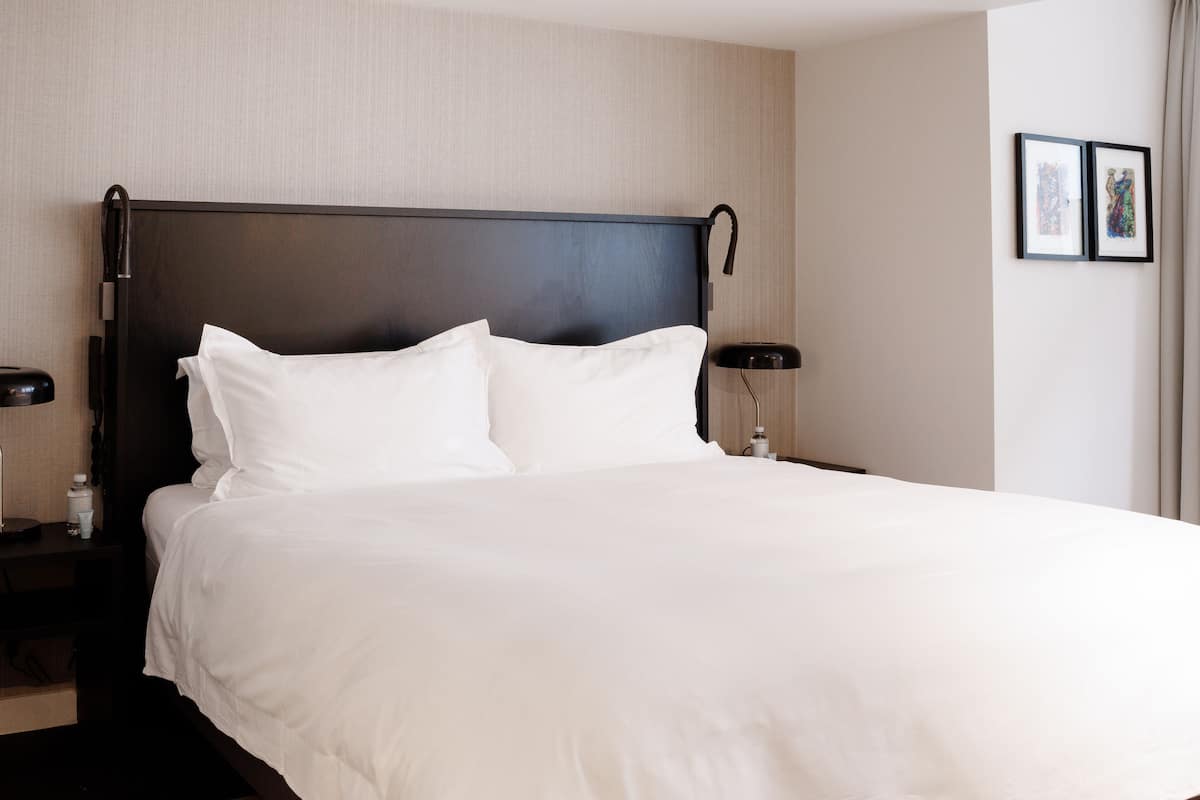Una cama bien hecha con sábanas blancas, un cabecero oscuro y dos lámparas de noche.