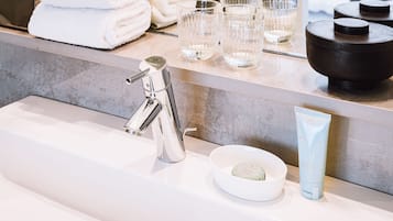 A modern bathroom with a chrome faucet, a white basin, a soap dish, and a tube of soap.